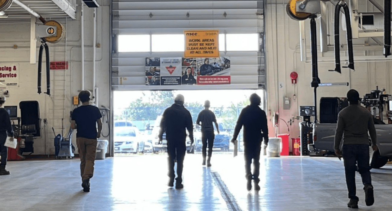 Cohort of 6 people in an automotive shop walking towards an open garage door